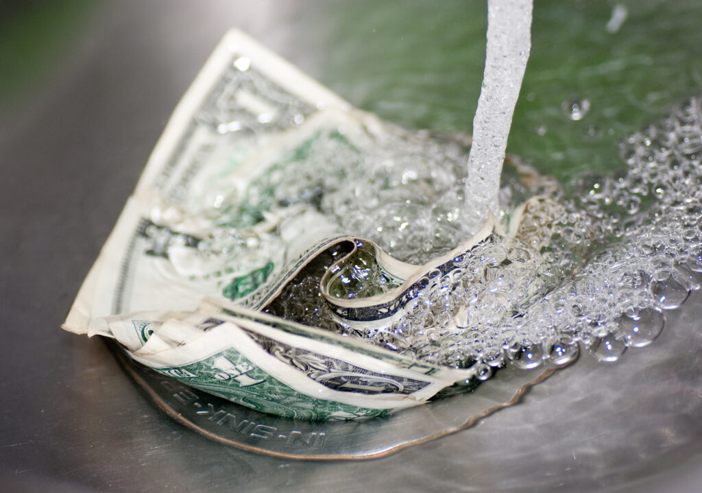 Close-up image of cash (bills or coins) swirling down a sink drain.